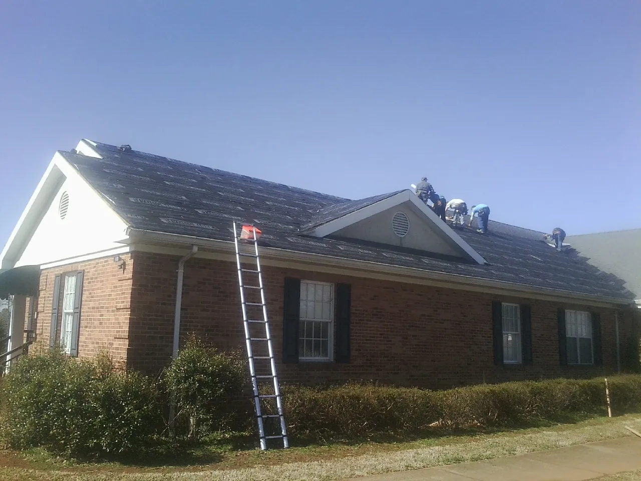Crew tearing shingles off a brick ranch roof with a ladder set — Emergency Roof Repair work by our crew in West Alexander