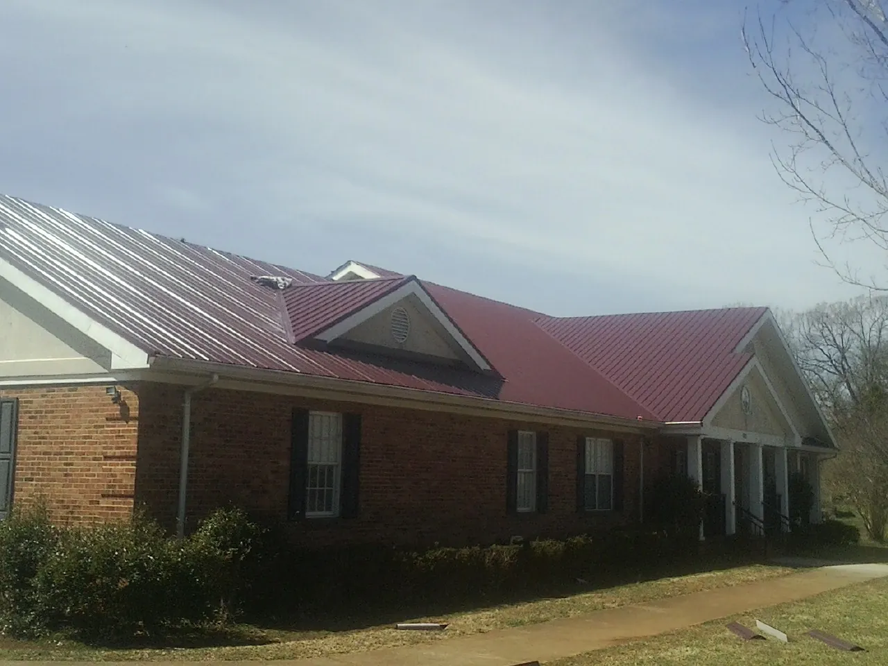 Red metal roof with gabled entries on a long brick building, from a Hail Damage Roof Repair job in West Alexander