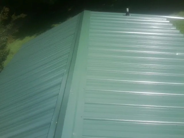 New green metal panels meeting at the ridge of a roof — Flat Roof Repair work by our crew in West Alexander
