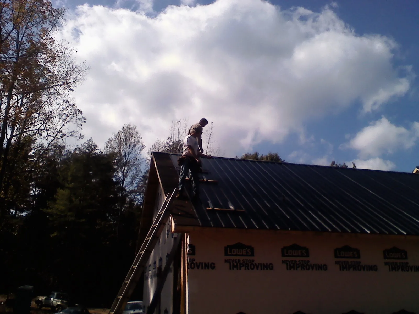 Roofer fastening dark metal panels high against a cloudy sky, from a Roof Inspection job in West Alexander