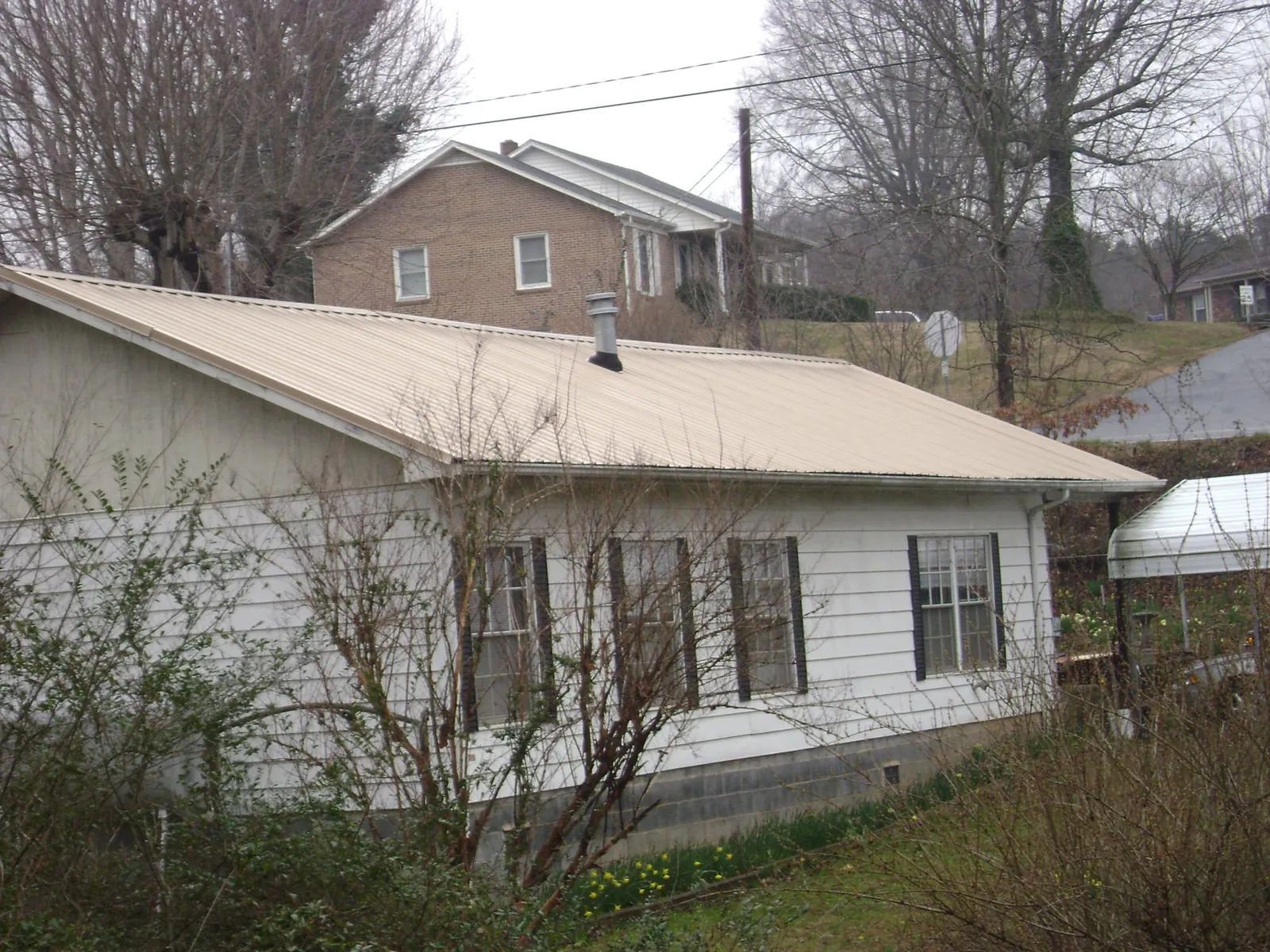 Tan metal roof on a white sided house set into a hillside — Commercial Roofing by Roofing Brothers in West Alexander
